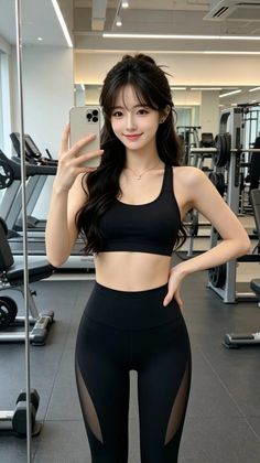 Woman in a black sports bra and leggings taking a mirror selfie in a gym