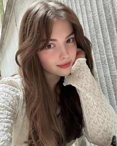 Woman with long brown hair wearing a white lace top, smiling softly