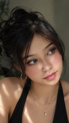 Woman with dark hair in an updo wearing gold jewelry and a black top