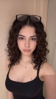 Woman with curly hair and glasses on her head wearing a black tank top