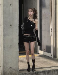 Woman in a black one-shoulder top and shorts standing outdoors