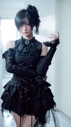 Person in a black gothic dress with ruffles and a headpiece posing indoors