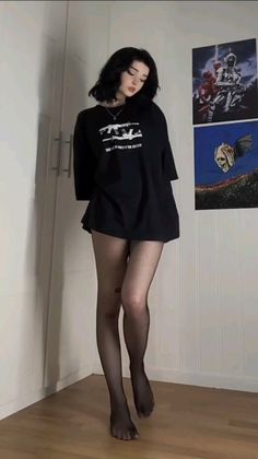 Woman with short black hair wearing an oversized t-shirt and fishnet stockings indoors