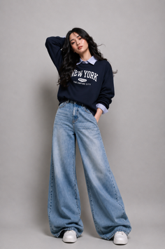 Woman in a navy sweatshirt and wide leg jeans posing in a studio