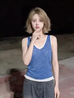 Woman with short blonde hair wearing a blue tank top and jeans against a dark background