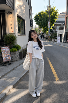 Woman in a white t-shirt and grey sweatpants standing on a street