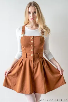 Woman with blonde hair wearing a brown overalls dress over a white long sleeve shirt