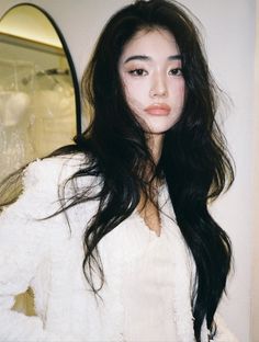 Woman with long black hair wearing a white top, looking at the camera