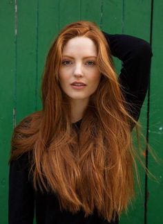 Woman with long red hair wearing a black top against a green background
