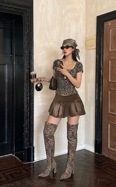 Woman in leopard print top and boots holding coffee and phone