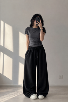 Woman in a gray t-shirt and black wide leg pants taking a mirror selfie