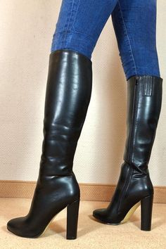 Person wearing black knee-high boots and blue jeans indoors