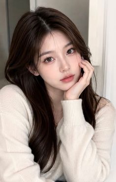 Woman with long brown hair wearing a white sweater, posing indoors