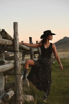 Woman in a cowboy hat and boots posing by a wooden fence at golden hour
