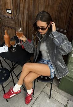 Woman in a leather jacket and plaid skirt sitting outdoors with a drink