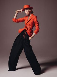 Woman in a red hat and blazer with wide leg pants posing in a studio