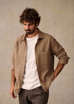 Man with curly hair and beard wearing a brown shirt over a white t-shirt