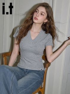 Woman with long wavy hair wearing a grey t-shirt and blue jeans, sitting indoors