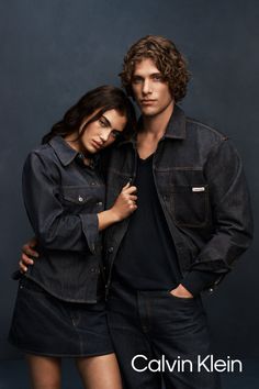 Two models in dark wash denim jackets and jeans against a dark background