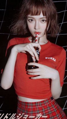 Woman with short hair in a red crop top and plaid skirt drinking from a Coca-Cola bottle