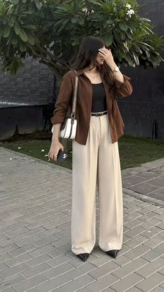 Woman in a brown shirt and wide leg pants holding a phone outdoors