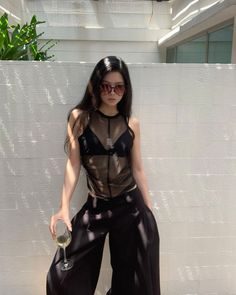 Woman in a sheer top and wide leg pants holding a glass outdoors