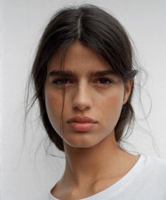 Woman with dark messy hair and natural makeup wearing a white t-shirt