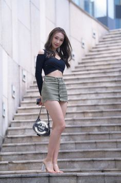 Woman in a black crop top and olive mini skirt standing on outdoor stairs