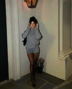 Woman in a gray sweater and shorts with tights and glasses outdoors at night