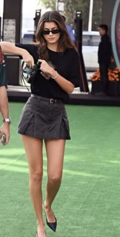 Woman with long hair and sunglasses wearing a black shirt and mini skirt outdoors
