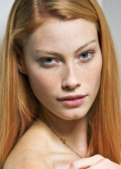 Woman with red hair and freckles wearing a necklace, looking directly at the camera