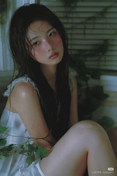 Woman with long dark hair and flushed cheeks in a white dress indoors