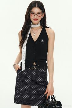 Woman with long hair and glasses wearing a black polka dot skirt and top