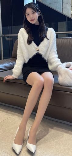 Woman with long hair wearing a white cardigan and black dress, sitting indoors