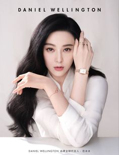 Woman with long black hair wearing a white shirt and watch in a studio setting