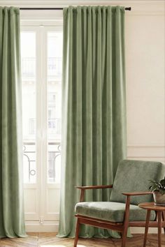 Green velvet curtains and an armchair by a window with a balcony view