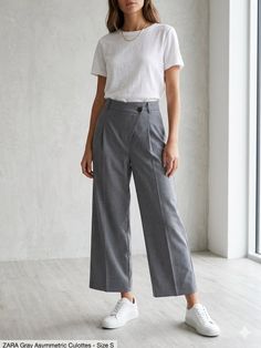 Woman in gray culottes and a white t-shirt standing indoors