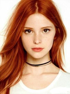 Woman with long red hair and freckles wearing a choker against a white background