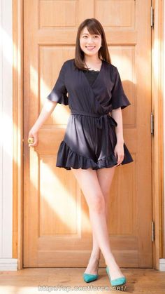 Woman in a black romper and teal heels standing in front of a wooden door