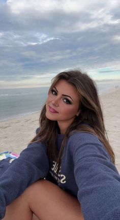 Woman with long hair in a blue sweatshirt smiling on a beach