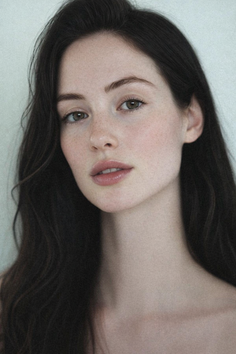 Woman with long dark hair and freckles in a soft-lit portrait