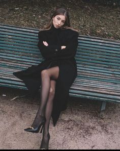Woman in a long black coat and tights sitting on a park bench