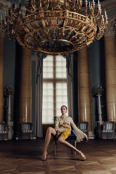 Woman in a ruffled top and yellow skirt sitting under a large chandelier