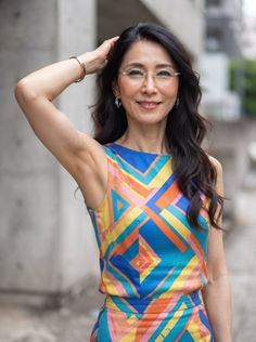 Woman with long dark hair and glasses wearing a colorful geometric top outdoors