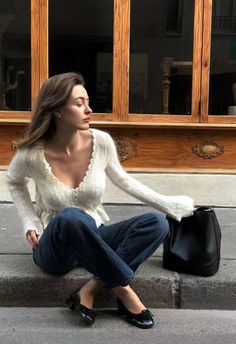 Woman with long hair wearing a white cardigan and jeans, sitting outdoors