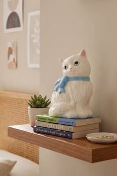 White cat figurine with a blue bow on a stack of books on a floating shelf