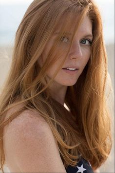 Woman with red hair and freckles looking over her shoulder outdoors