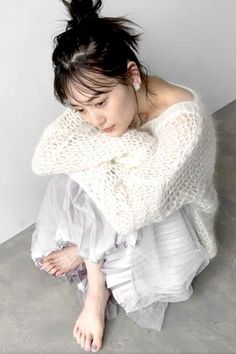 Woman in a white knit sweater and pleated skirt sitting on the floor