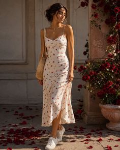 Woman in a white floral dress and sneakers standing next to red roses