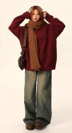 Person with red hair wearing an oversized sweater, plaid scarf, and baggy jeans